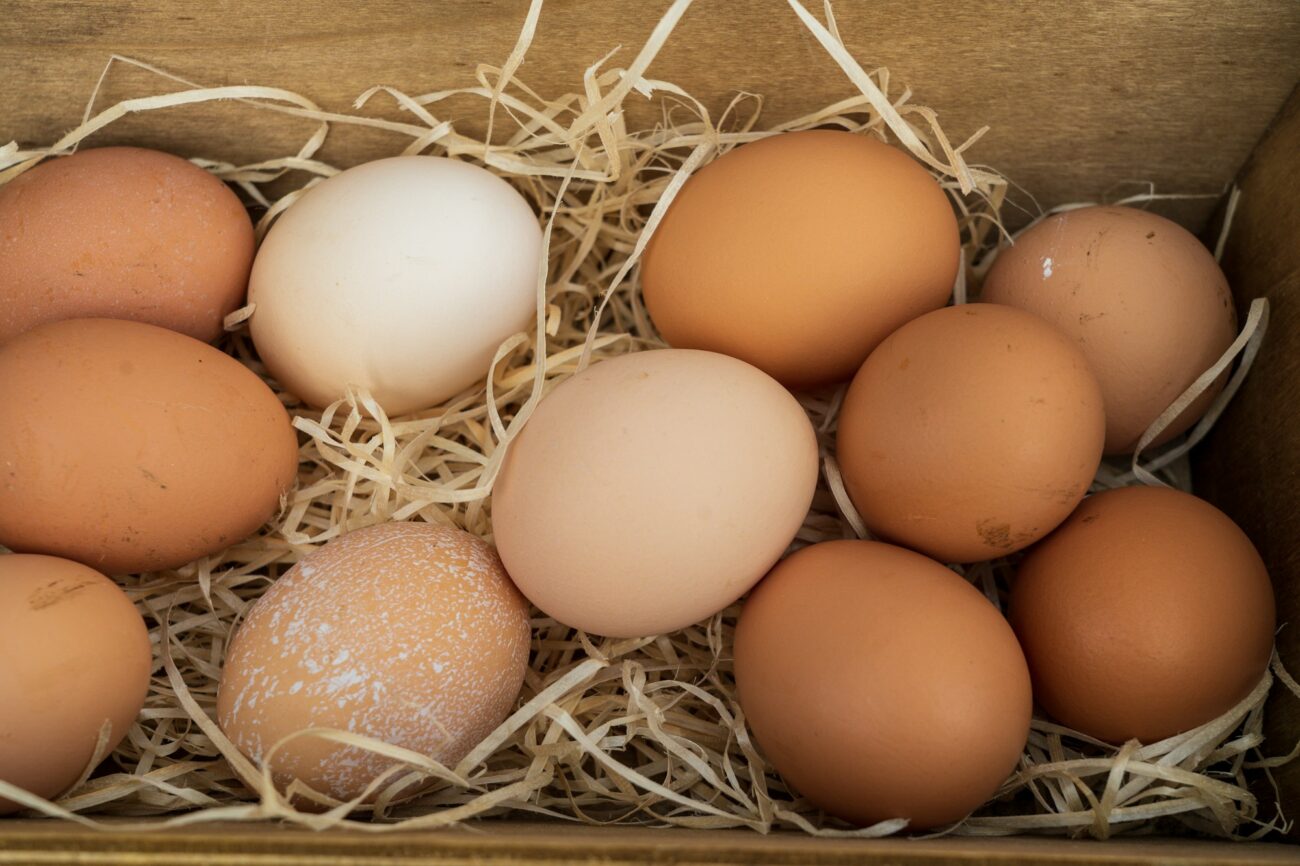 Brown, tan and cream eggs resting on straw in a wooden nest box